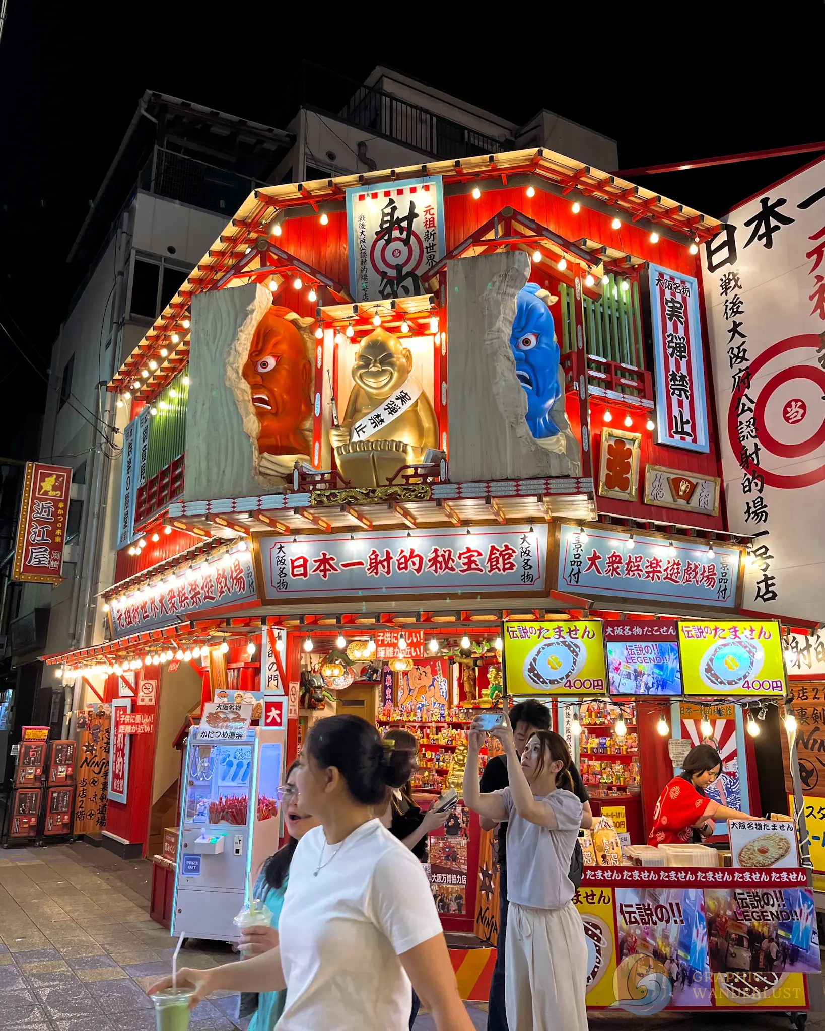 Gaudy Japanese storefront with striking 3D displays and with people passing and taking pictures infront.