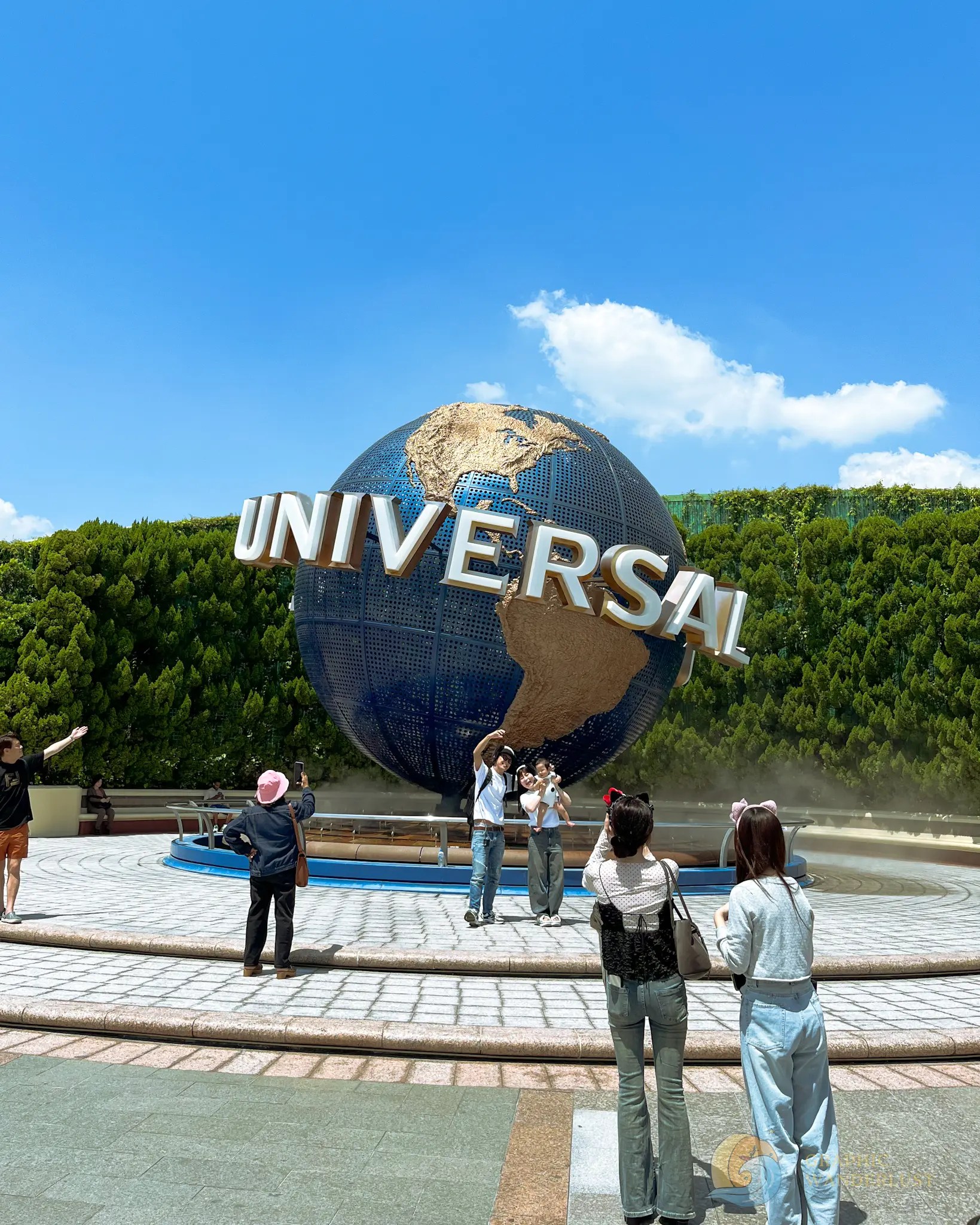 Universal Studios Japan Logo People taking photos and posing in front of a large Universal globe sculpture under a clear blue sky