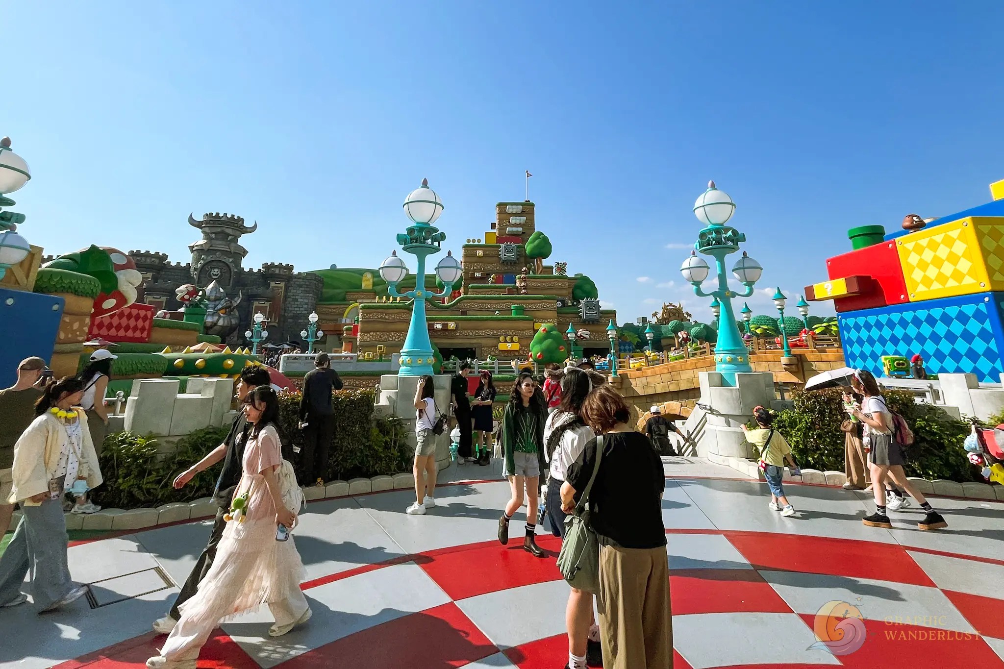 Universal Studios Japan Super Nintendo World People walking and taking photos in an outdoor theme park area designed with large colorful blocks and castle-like structures inspired by a video game
