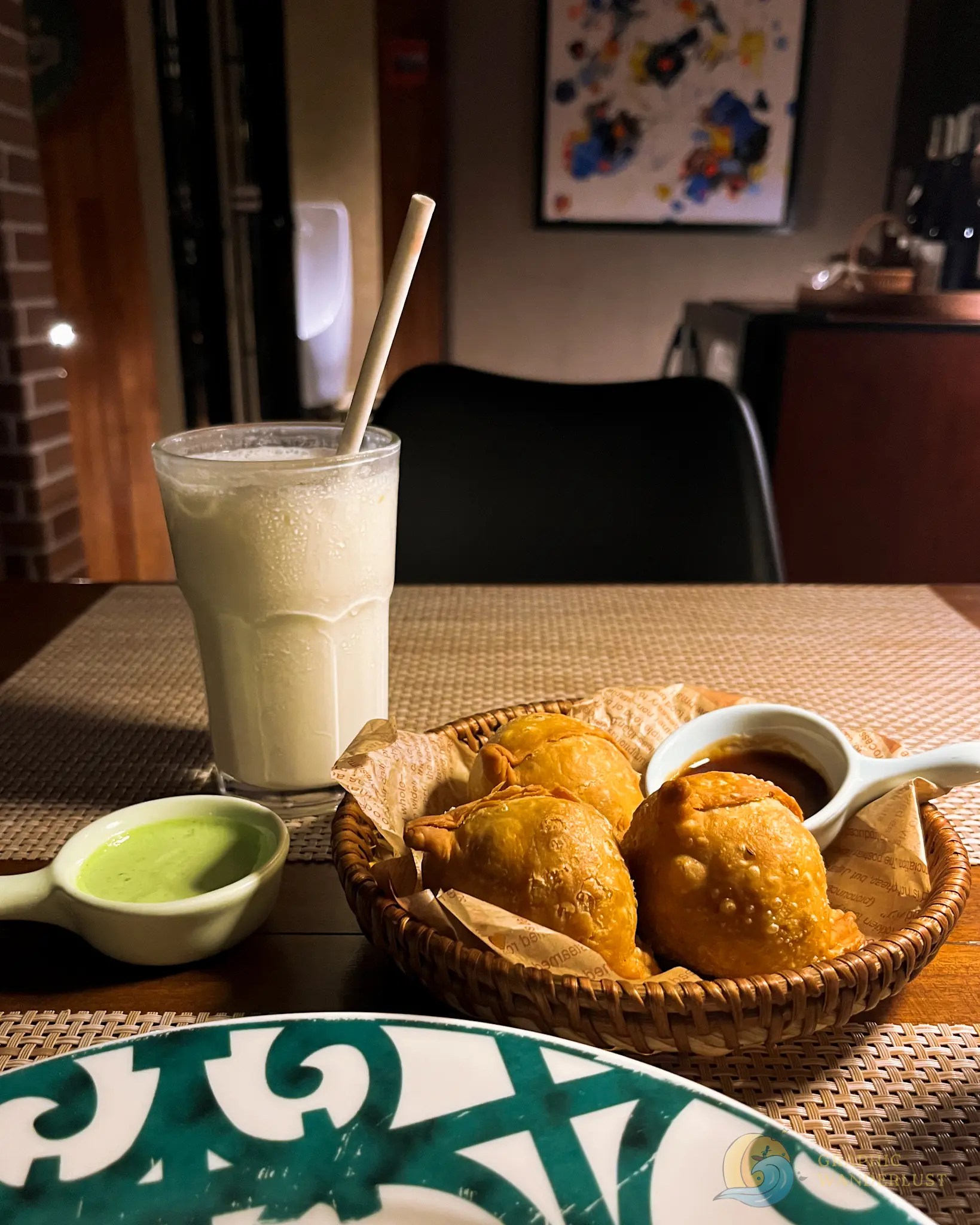 Basket of savory pastries with dipping sauces and a creamy drink on a restaurant table