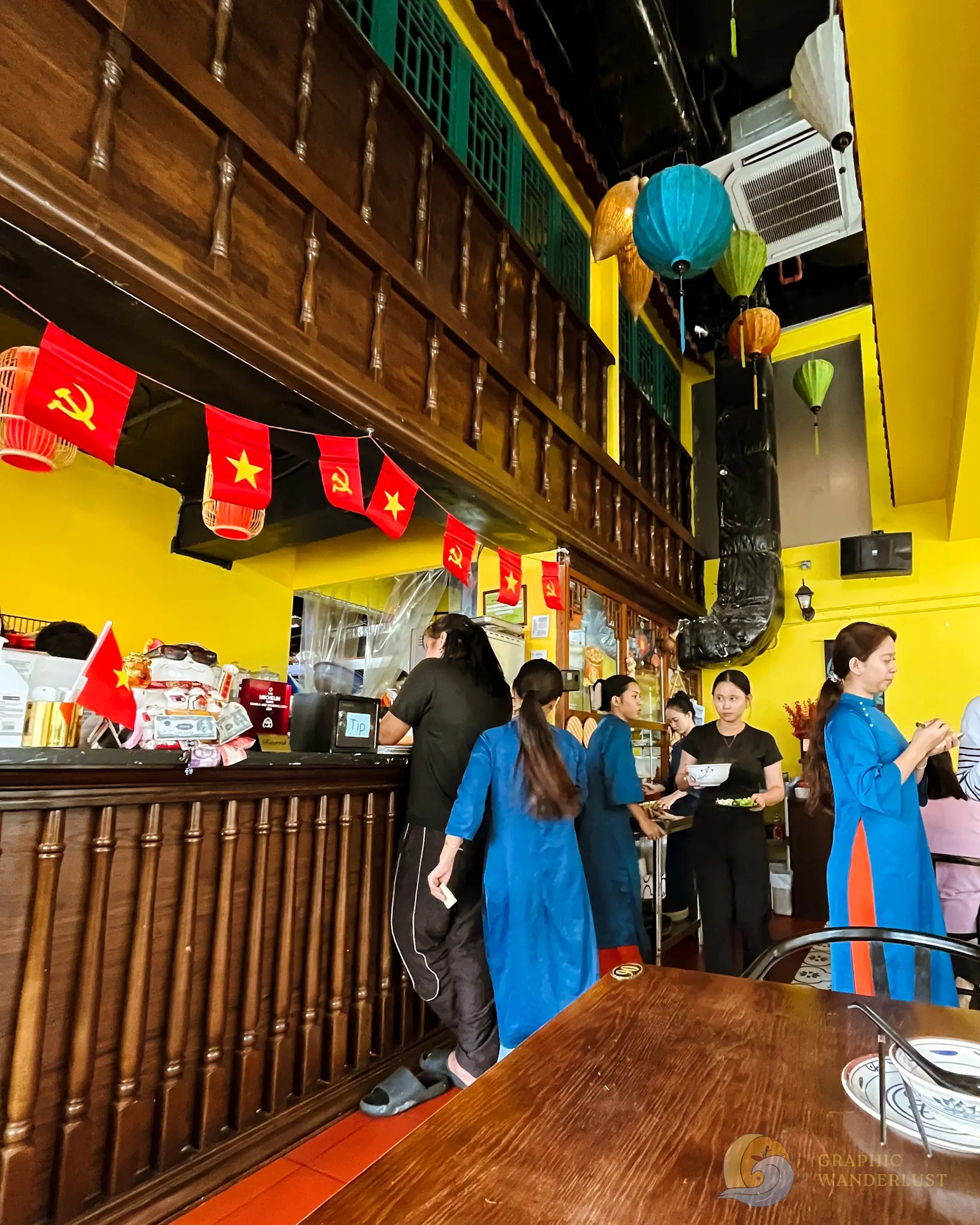Busy Vietnamese restaurant with colorful lanterns, flags, diners, and staff