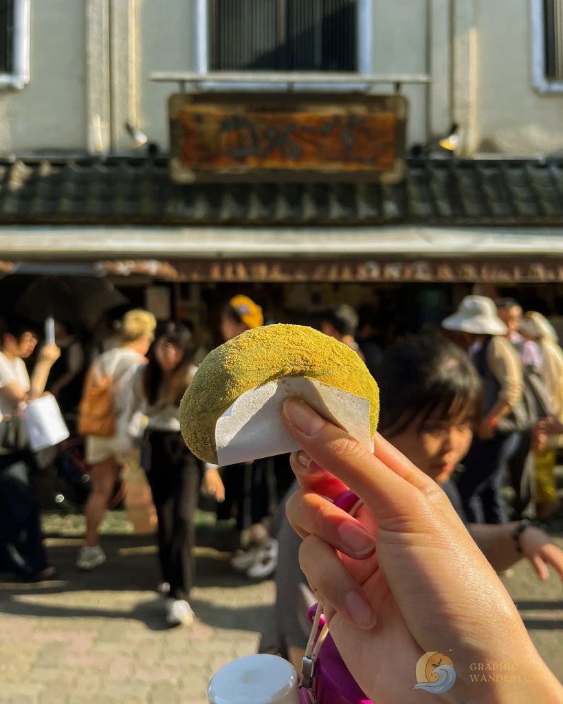 Hand holding a yellow powder-coated snack with a crowd and a building in the background