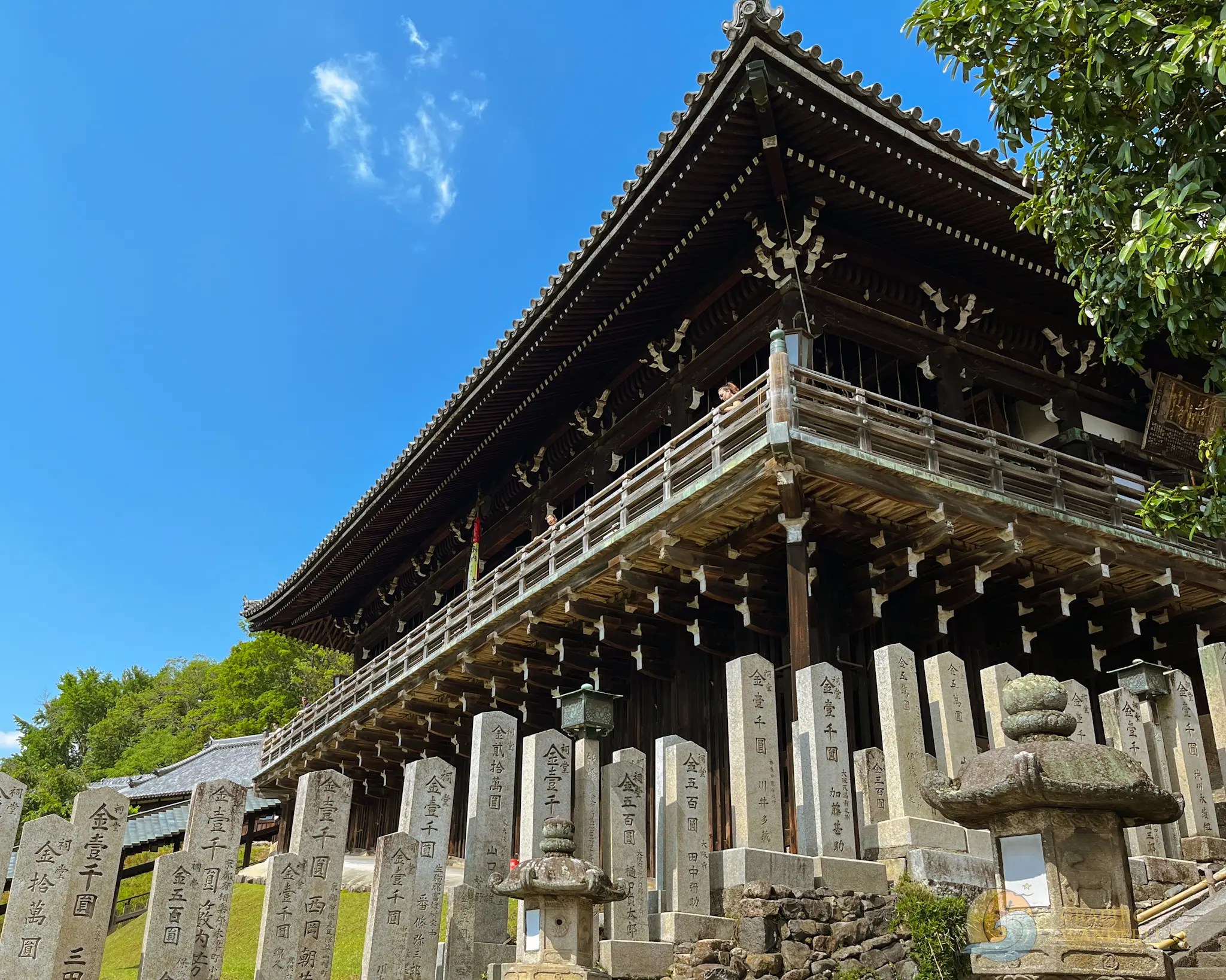 A building in Japanese architecture with a background of clear blue sky and series of rock blocks with Japanese characters below it.