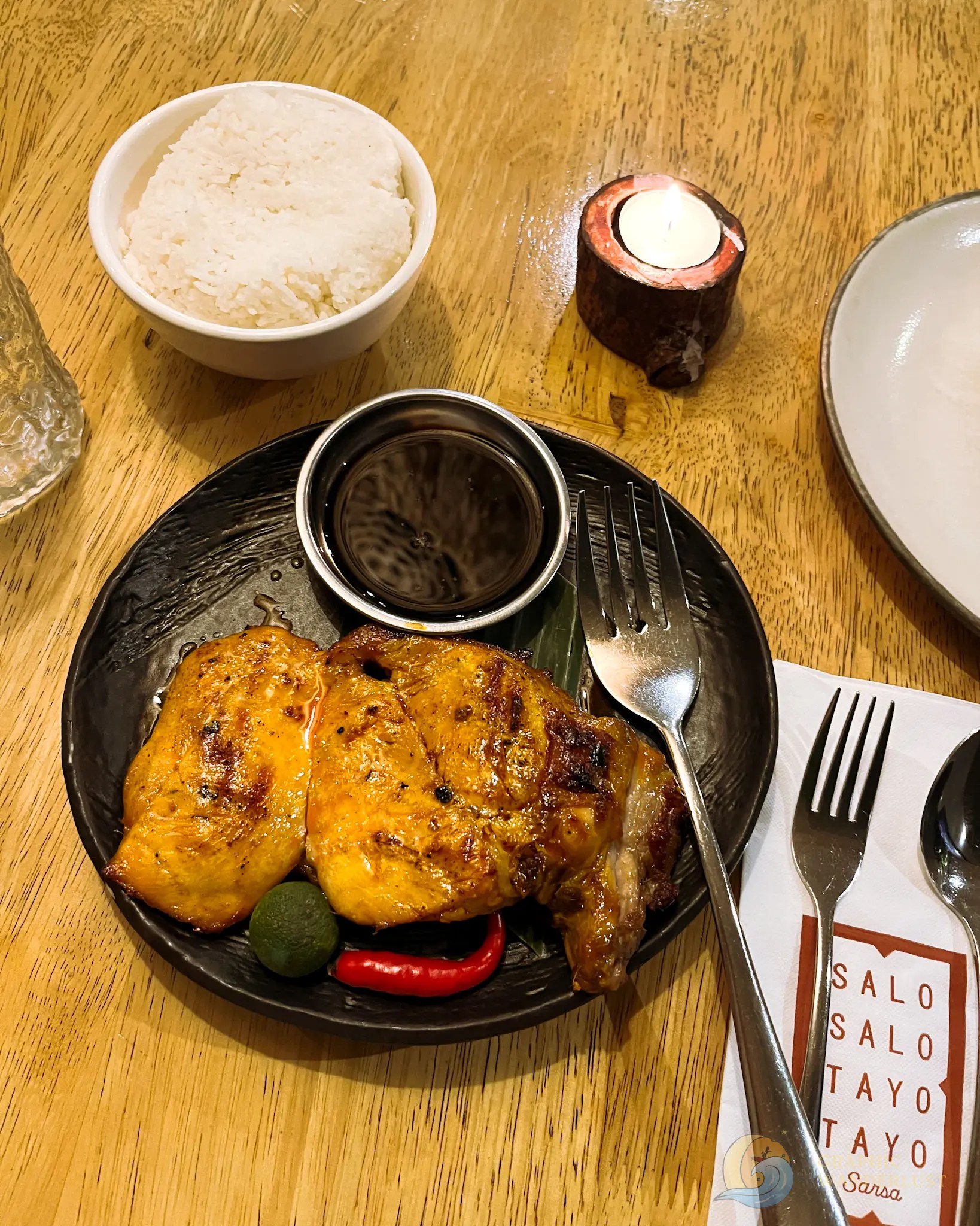 Grilled chicken with rice, dipping sauce, chili, and lime on a restaurant table