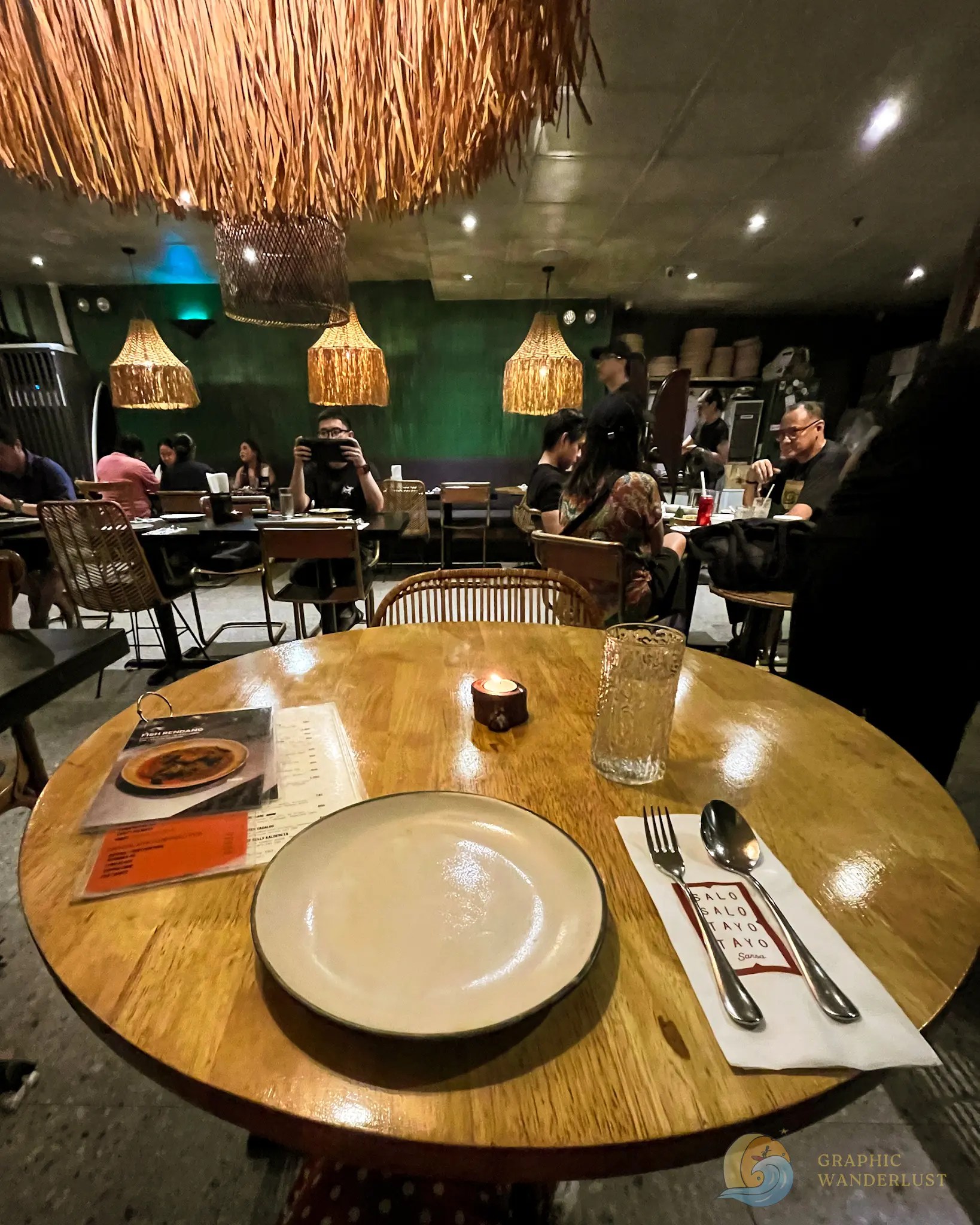 Busy restaurant dining room with thatched pendant lamps and a set table