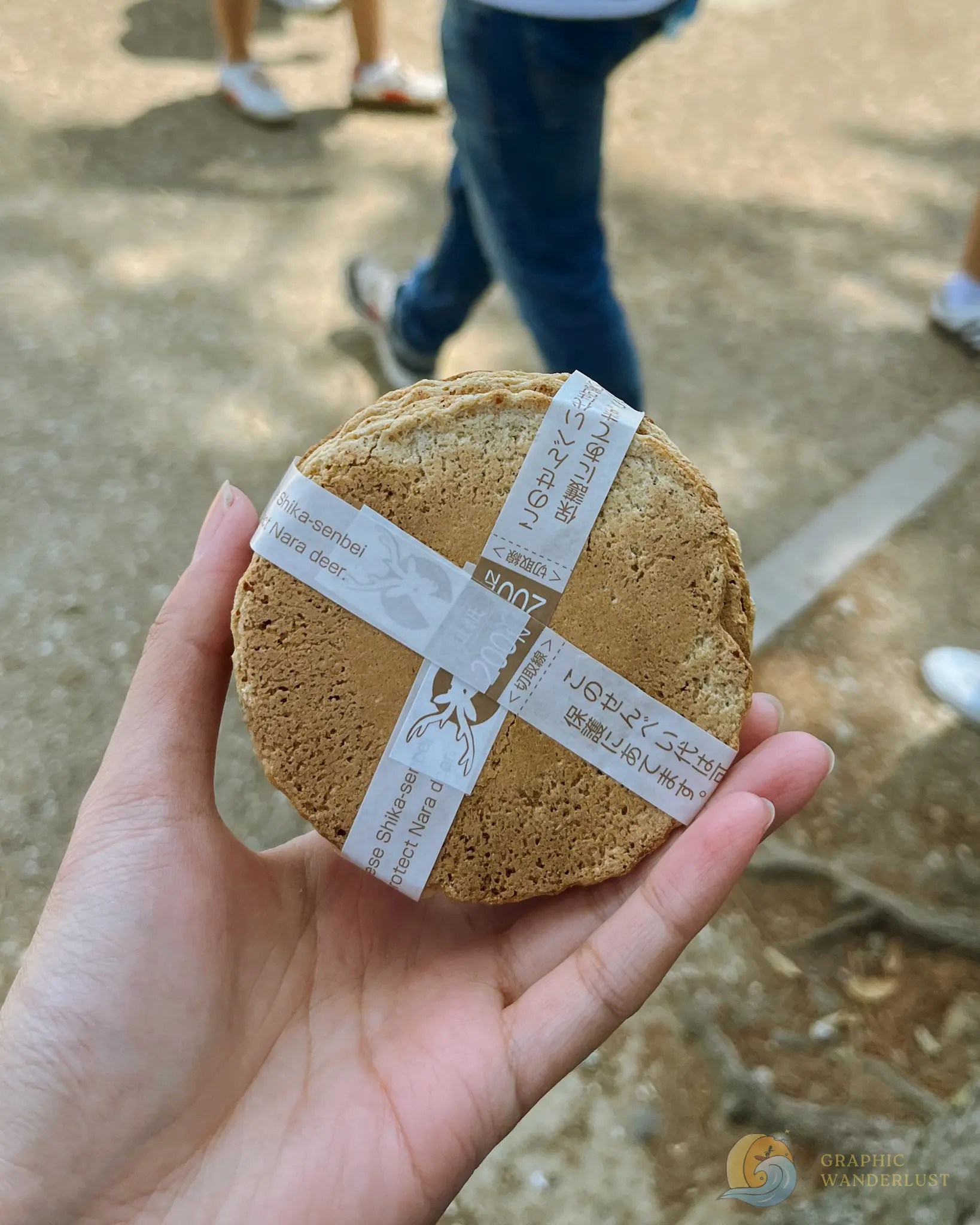 Hand holding a round Japanese snack wrapped with paper strips containing Japanese text