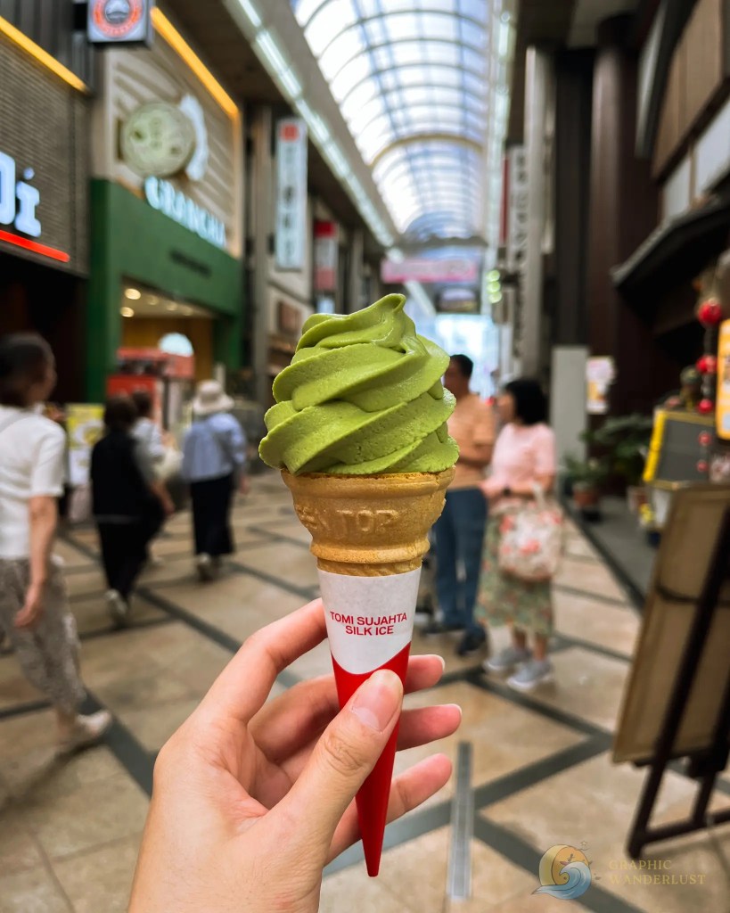 Hand holding green matcha soft serve ice cream cone inside a shopping arcade