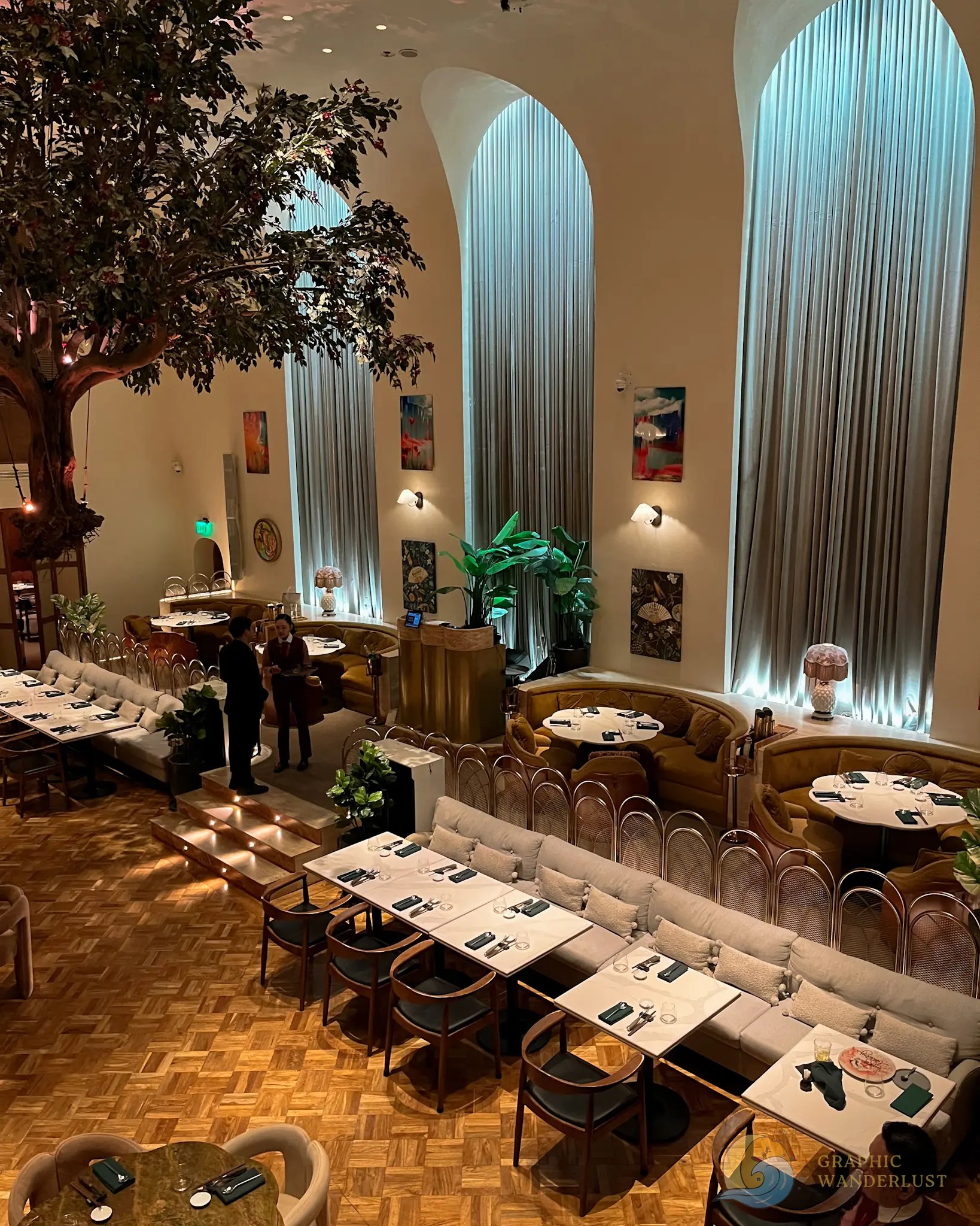 Elegant restaurant dining room with arched windows, plants, artwork, and set tables