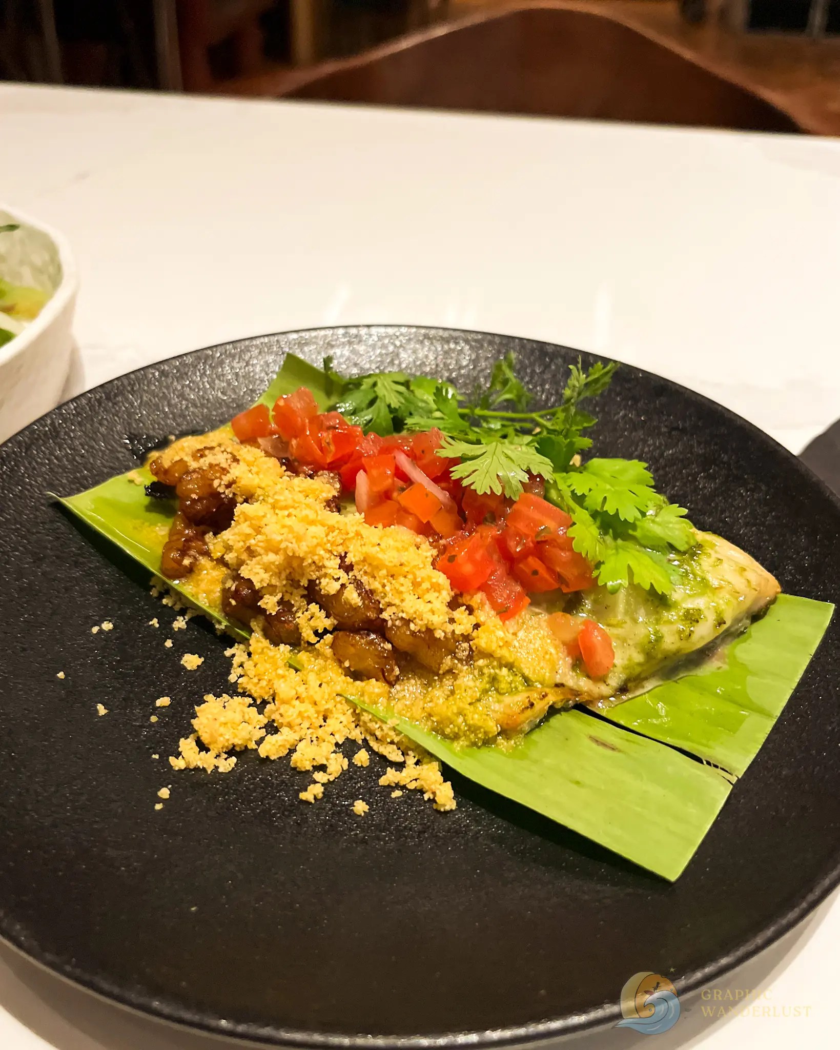 Grilled stuffed vegetables topped with tomatoes, herbs, and crunchy crumbs on a banana leaf