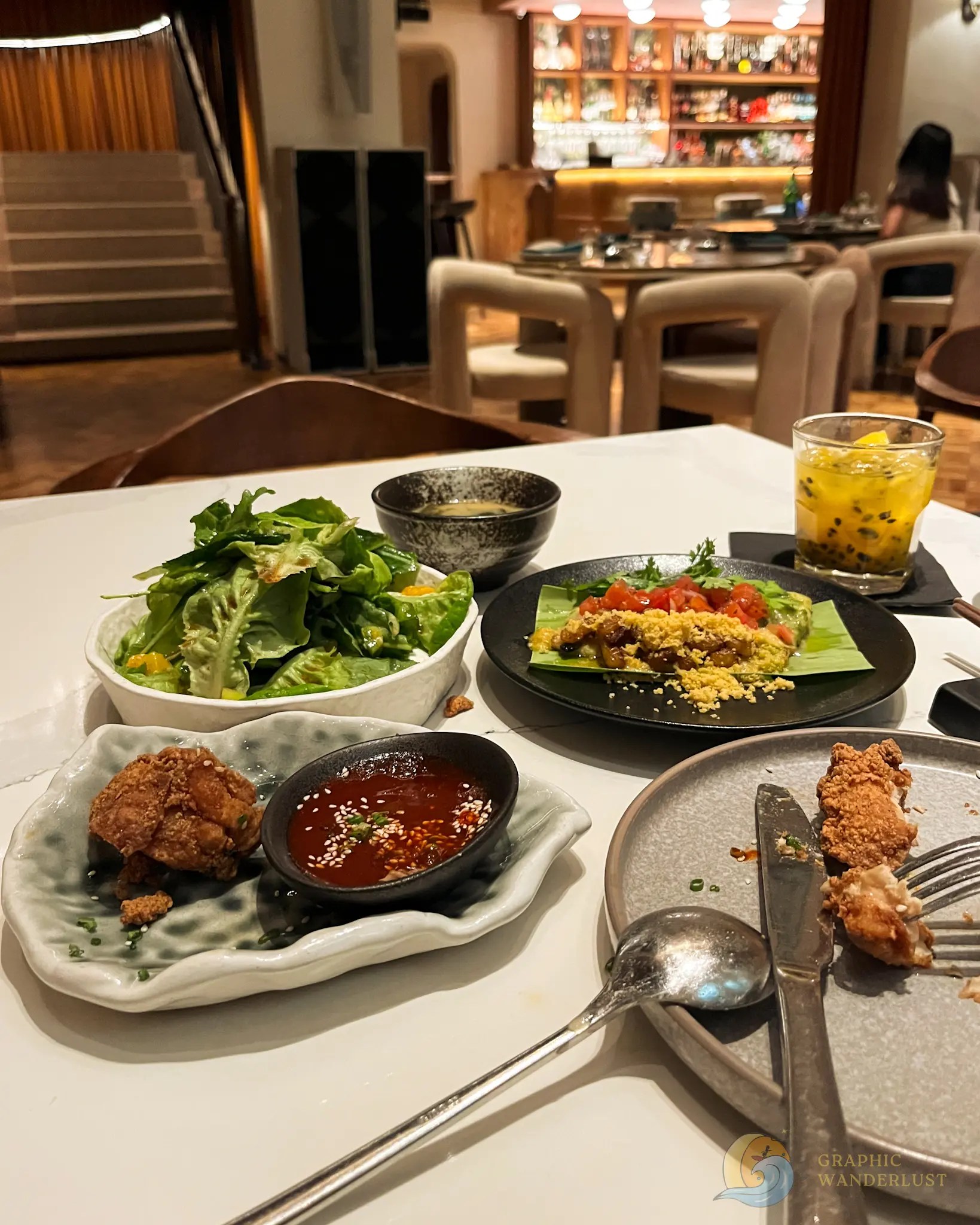 Asian dishes, salad, dipping sauce, and passion fruit drink on a restaurant table