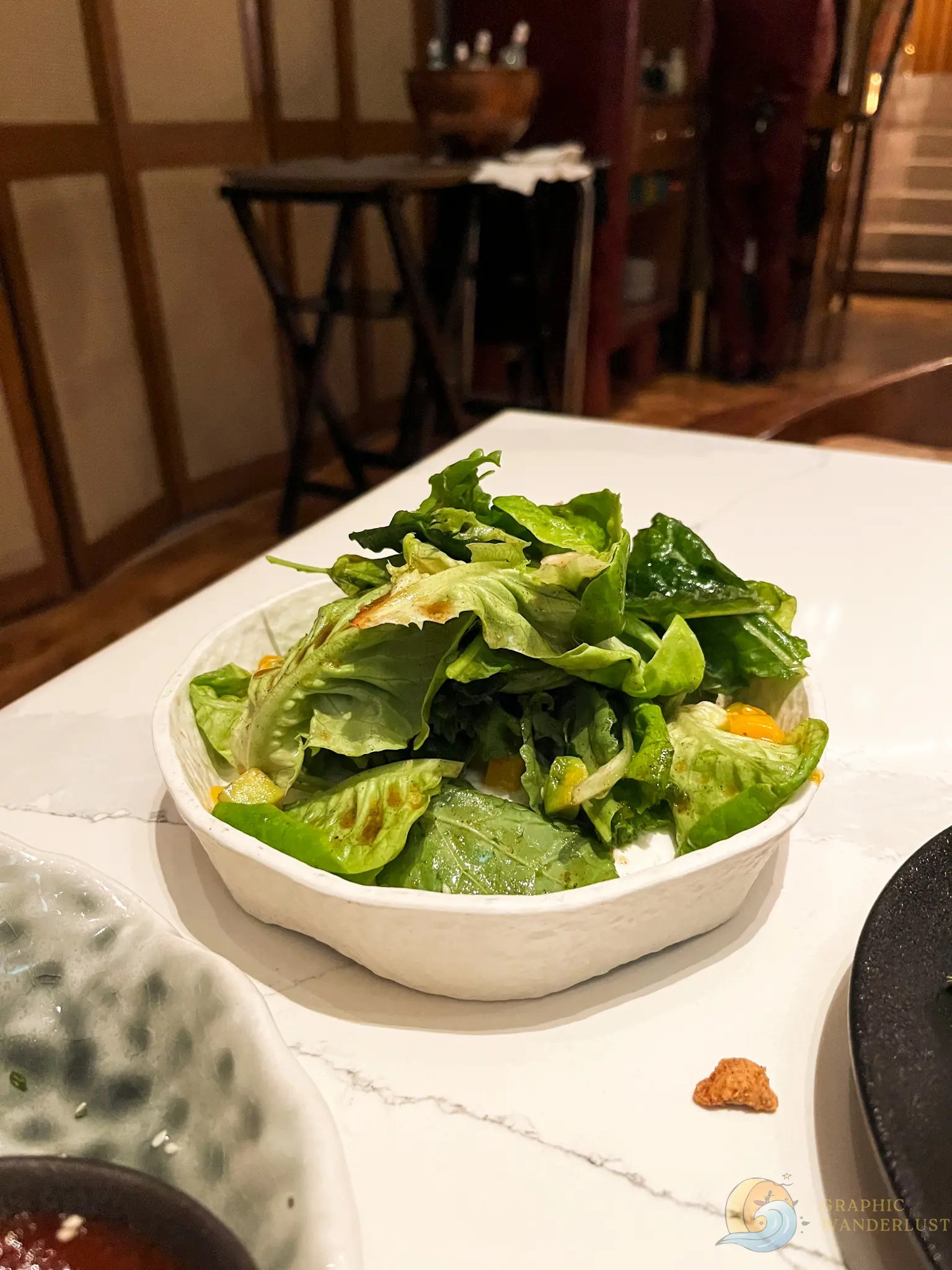Bowl of fresh green salad with tomatoes and dressing on a restaurant table