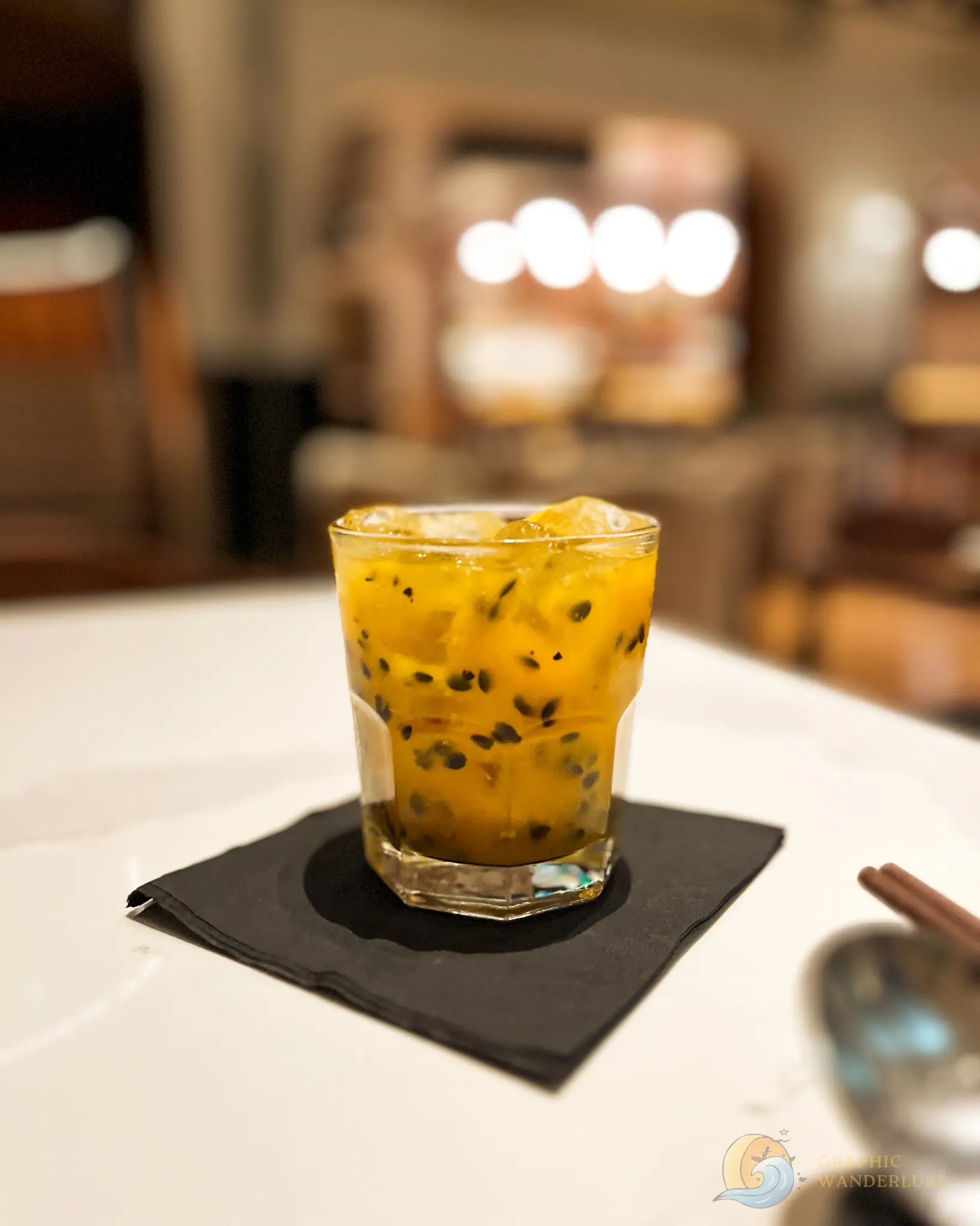 Uman Nota Manila Yellow Fever Mocktail Passion fruit drink with ice in a glass on a black napkin